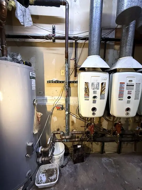 Mechanical room with a large tank water heater and two wall-mounted water heaters connected to metal vent pipes and copper piping.