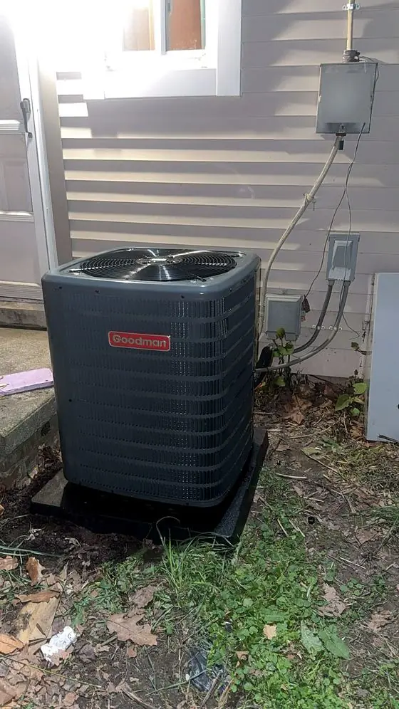 Outdoor air conditioning condenser on a pad beside gray siding, near the electric meter and disconnect box.