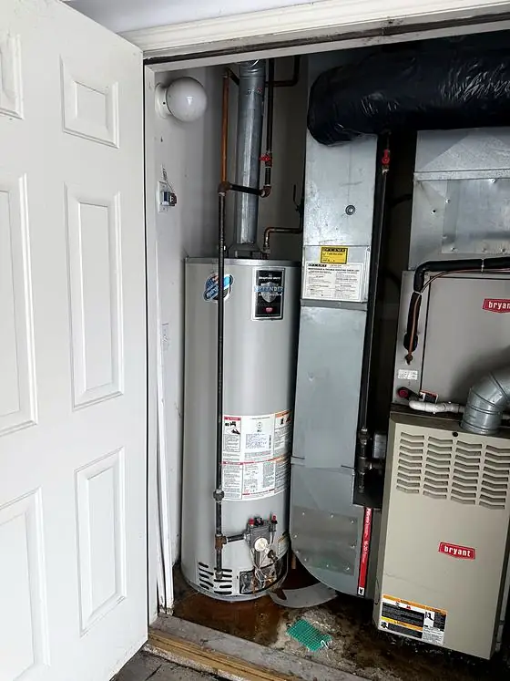 Equipment detail: utility closet holding a gas tank water heater beside a furnace and ductwork. Water is visible on the floor.