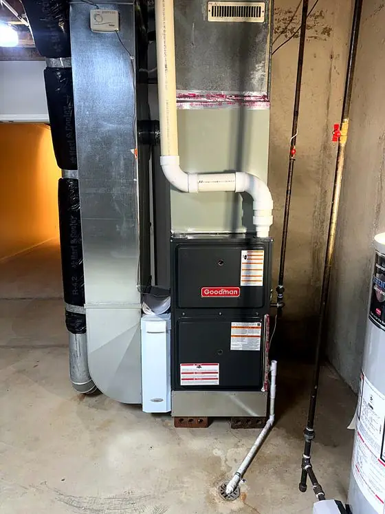 Furnace with white PVC vent pipes, sheet-metal ductwork and a condensate drain line in an unfinished basement.