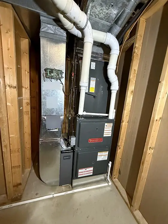 Furnace with white PVC vent pipes, a tall sheet-metal duct and a filter cabinet in a framed basement utility space.
