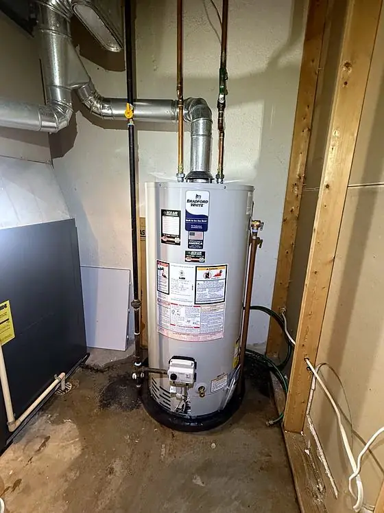 Gas tank water heater with copper water lines, a metal flue and Eco Air service labels in a basement utility area. Floor staining is visible.