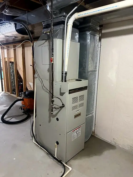 Upright gas furnace with white PVC vent pipe, a gas line with red shutoff valve and sheet-metal ductwork in an unfinished basement.