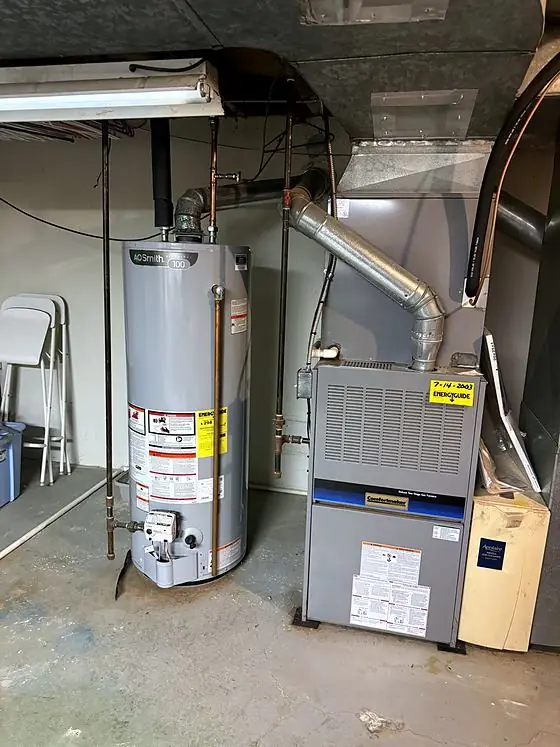 Gas tank water heater beside a two-stage gas furnace with metal vent pipes, an air cleaner cabinet and ductwork in a basement utility area.