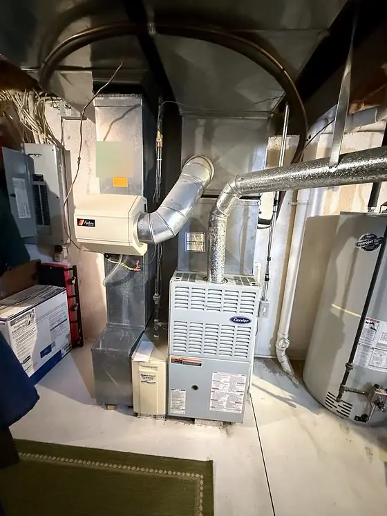 Gas furnace with metal flue pipe, a duct-mounted humidifier and a media air cleaner cabinet, next to a gas water heater in a basement.