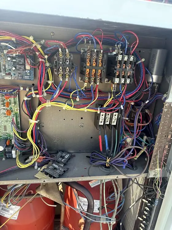 Equipment detail: open control panel of a large outdoor unit showing circuit boards, contactors, a capacitor and bundled wiring above the compressors.